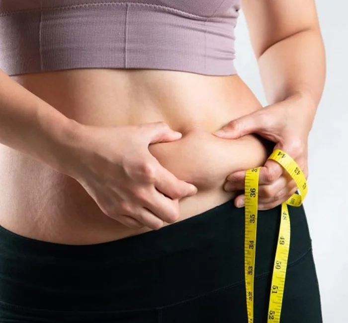 Woman measuring stubborn belly weight with a tape measure