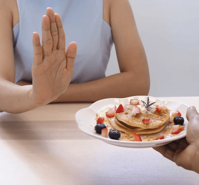 Woman turning down a plate of pancakes to control cravings